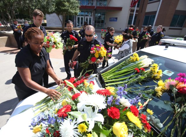 Dallas Police officers lay flowers on a squad car parked outside headquarters on Lamar Street today, in memory of those slain in Thursday's ambush. (Photo: Chris McGathey/Newscom)