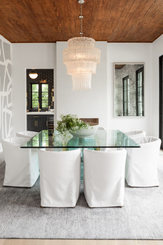 She used a wood wallpaper to line the dining room ceiling, creating cohesiveness with the wood in the rest of the home and selected Porter Teleo’s Tangled pattern on a wall. Relaxed chairs from Restoration Hardware cement the coastal vibe and pair nicely with a table from Scout Design Studio. The Oly chandelier and an antiqued mirror from Ochre add elegance to the room.