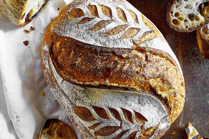 A loaf of rustic sourdough bread with leaf-pattern scoring on the crust.