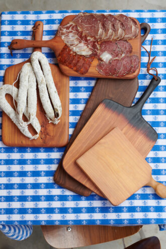 Wood serving boards with charcuterie on top, all spread on a blue and white checkered tablecloth.