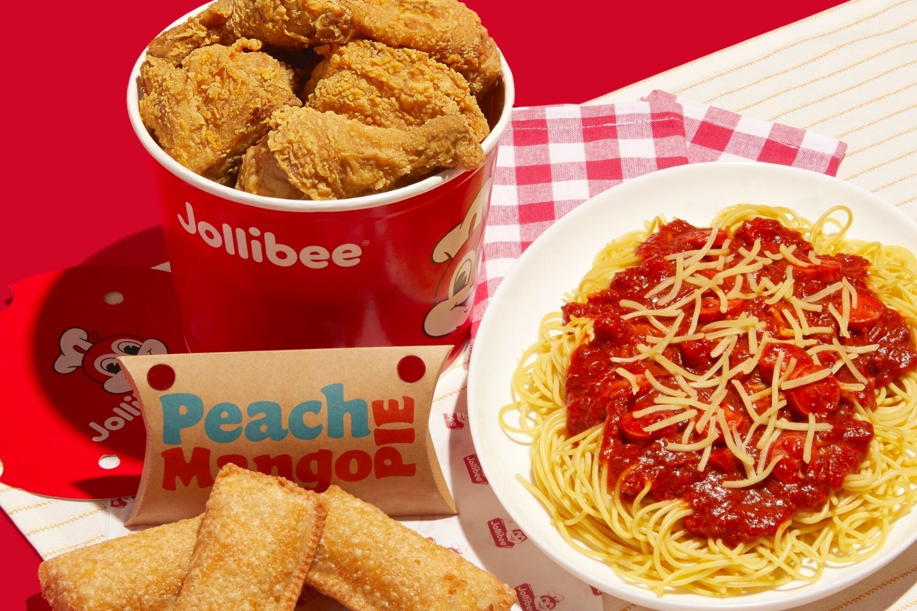 Fast-food spread from Jollibee with a bucket of Chickenjoy fried chicken, mango peach hand pies, and a plate of spaghetti.