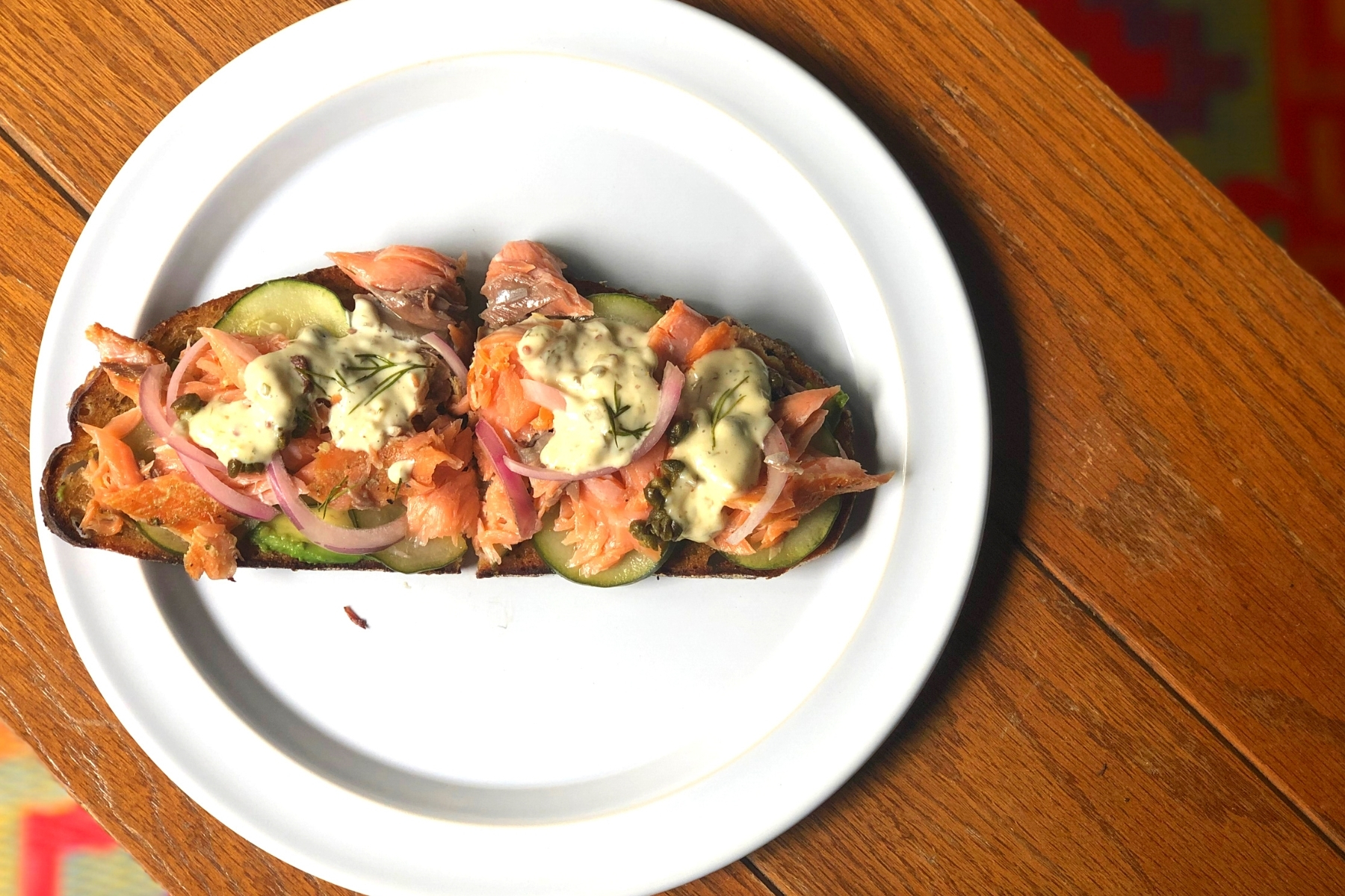 A white plate on a wood table, on the plate: an open-face tartine with smoked salmon.