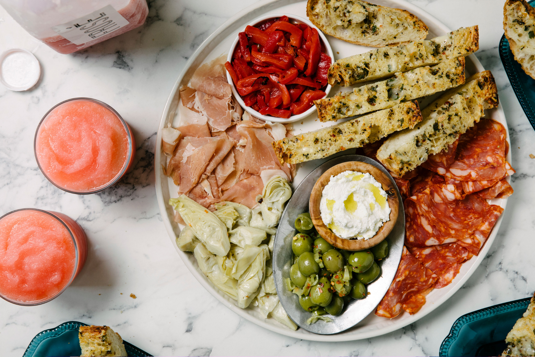 A big platter filled with bread, olives, spreads, cured meats, and cheeses; beside it, a glass of frozen rosé.