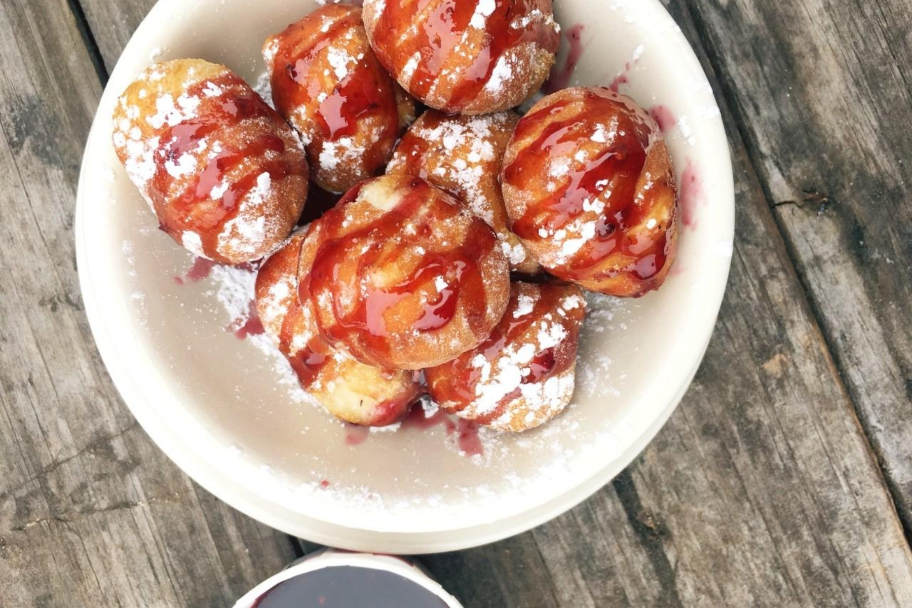 A white plate with a dessert called Goat Balls: fried biscuit dough wrapped around brie cheese, dusted with powdered sugar, and drizzled with strawberry sauce.