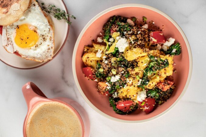 A pink bowl with a breakfast scramble inside, served with veggies and quinoa.