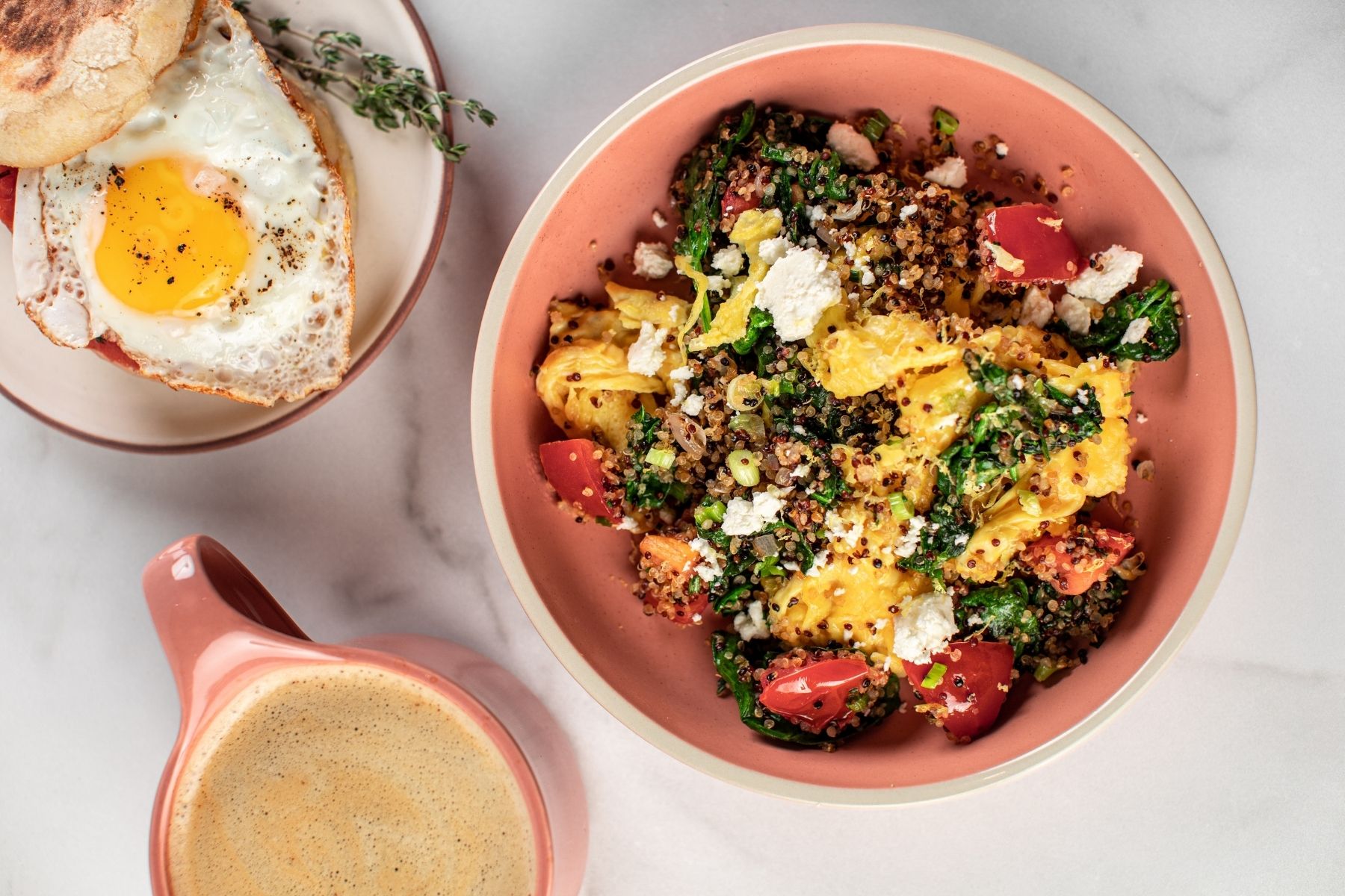 A pink bowl with a breakfast scramble inside, served with veggies and quinoa.