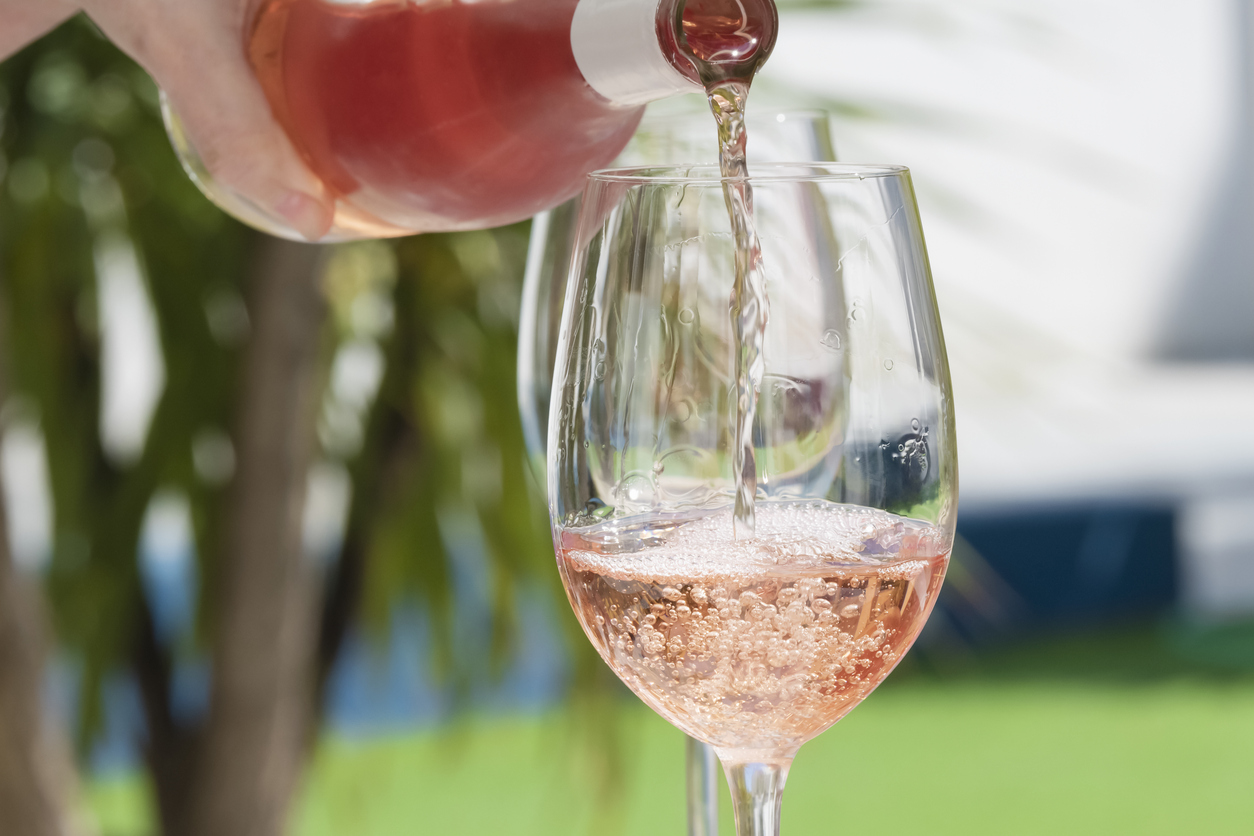 close up of a hand pouring delicious rose wine from bottle into glass outdoors.