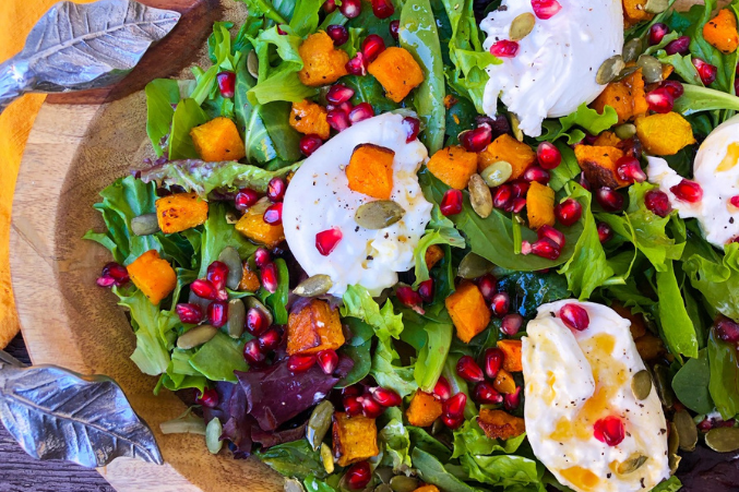 A zoomed in image of salad with pumpkin seeds, pomegranate seeds, and soft burrata cheese.