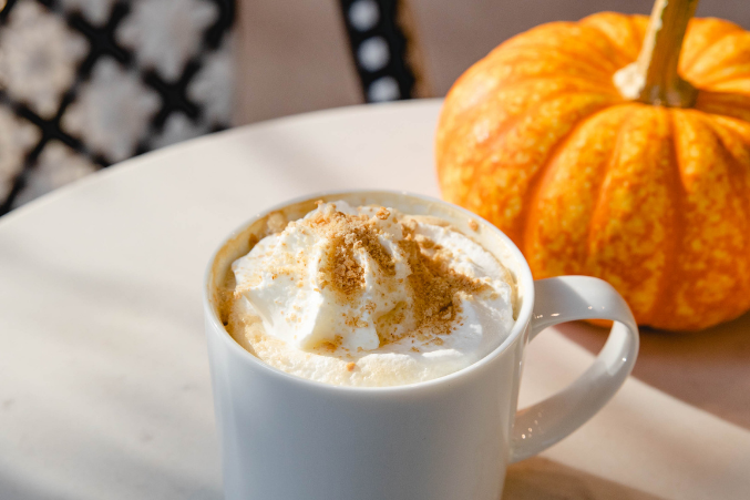 A pumpkin spice latte on a table next to an actual pumpkin.