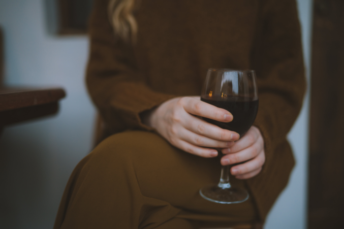 A woman in a brown sweater and pants holding a glass of red wine.
