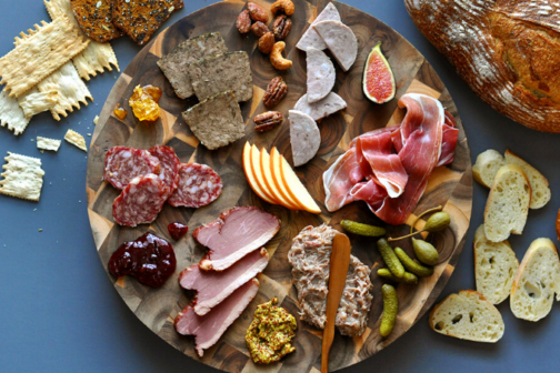 A charcuterie and cheese board spread on top of a wood platter.