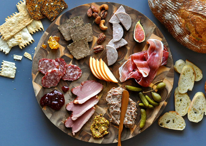 A charcuterie and cheese board spread on top of a wood platter.