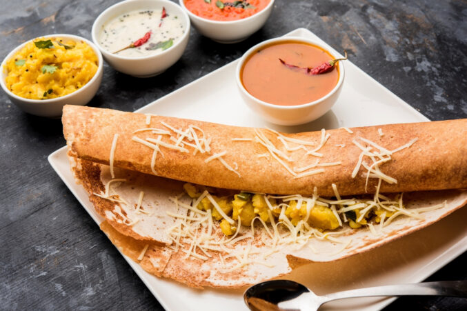 A plate of dosa, an thin, savory Indian crepe, with various cups of side sauces.