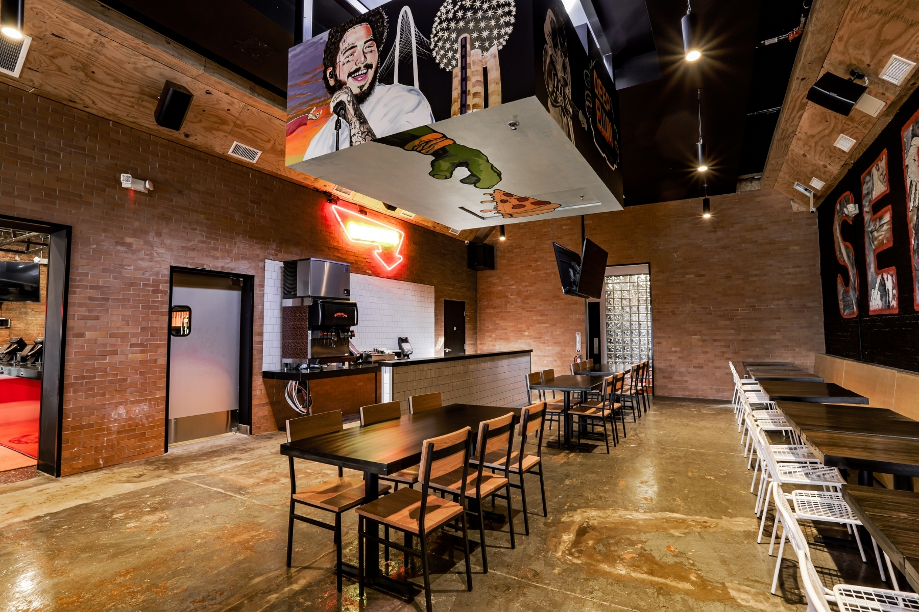 The empty, remodeled interior of Serious Pie in Deep Ellum. A painted mural of Post Malone linger over a table with chairs in the middle of a dining room.