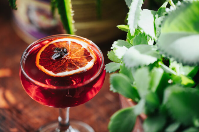 A deep red cocktail made with rye whiskey, garnished with a dried orange wheel.