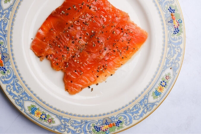 A vibrant orange filet of smoked salmon on a plate with ornate vintage perimeter.