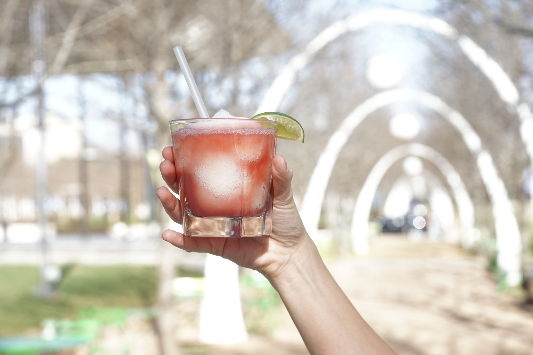 A White hand holds up a glass of frozen margarita with a lime wedge.