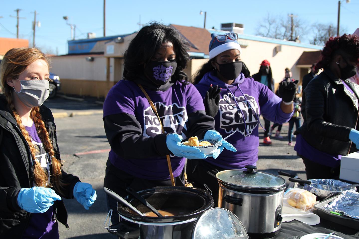 Three women wearing gloves and masks, serving hot meals to those in need in South Dallas.