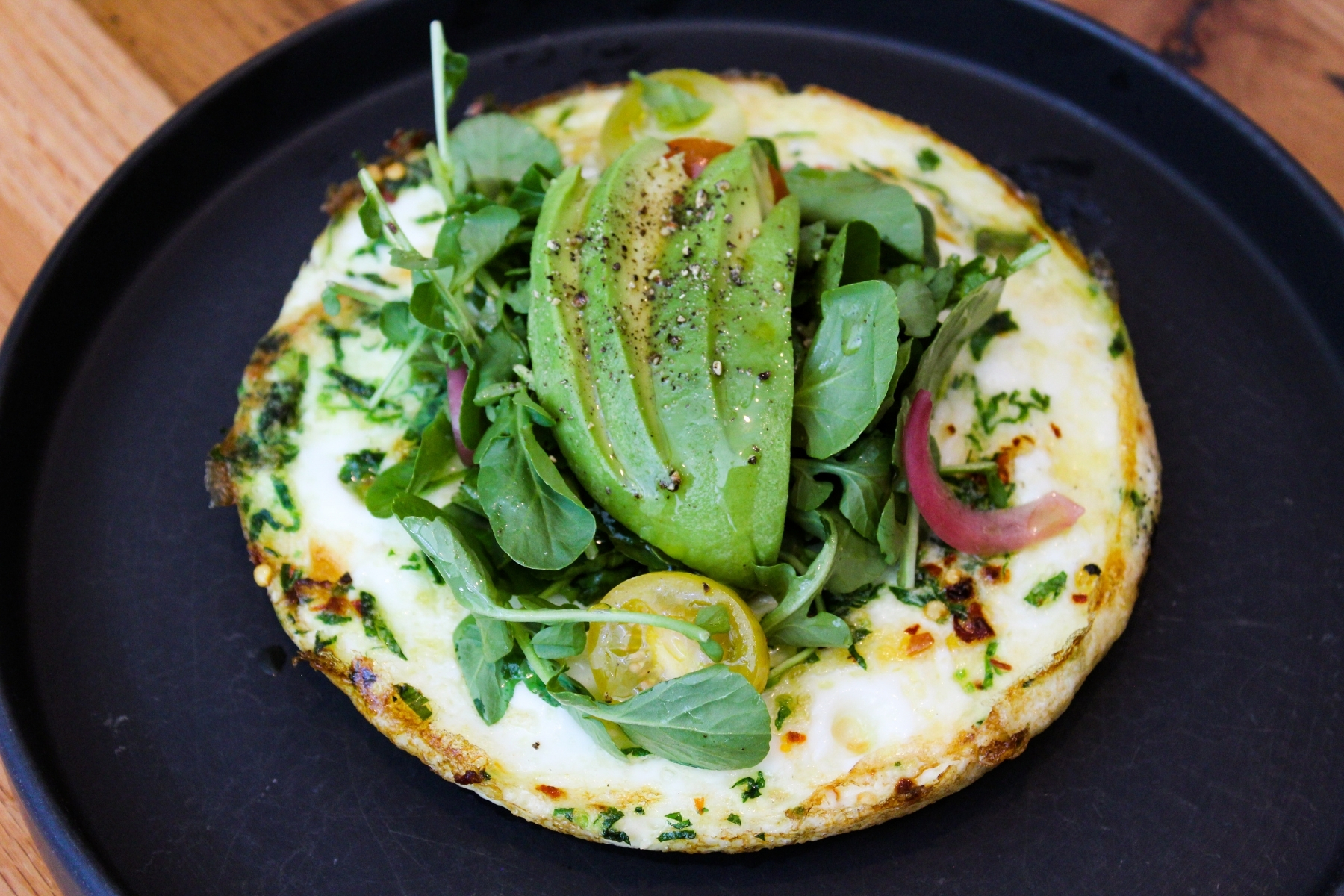 A round egg white frittata topped with greens and avocado slices.