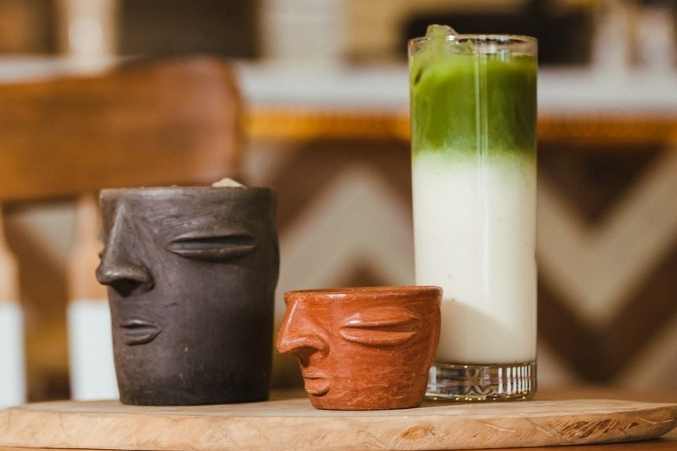 A row of three coffee drinks: horchata in a clay cantarito, espresso in a smaller cantarito, and a tall glass of matcha horchata.