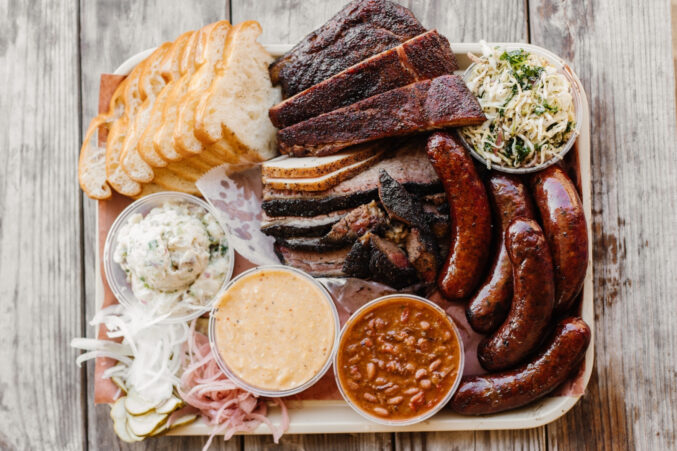 A packed tray of barbecue (ribs, links, beans, mac, slaw, bread) from Goldee's Barbecue