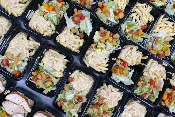 A table full of to-go containers filled with pasta and salad.