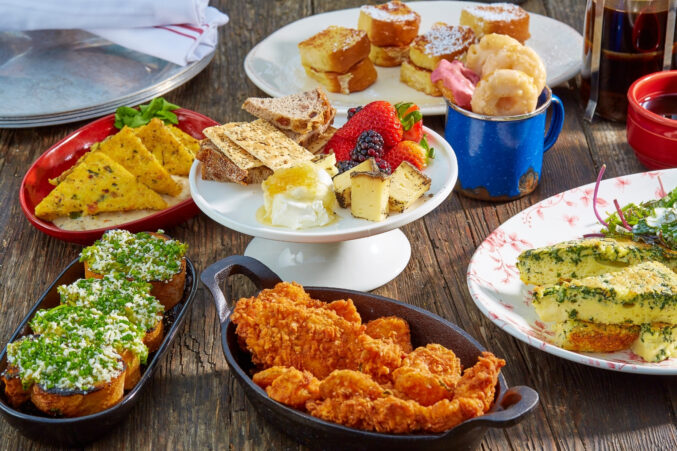 A table of brunch foods like avocado toast, hot chicken, msoked grits, doughtnuts, and baked eggs.