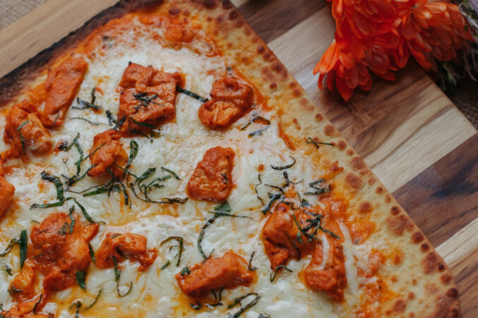 Thin-crust pizza topped with butter chicken.