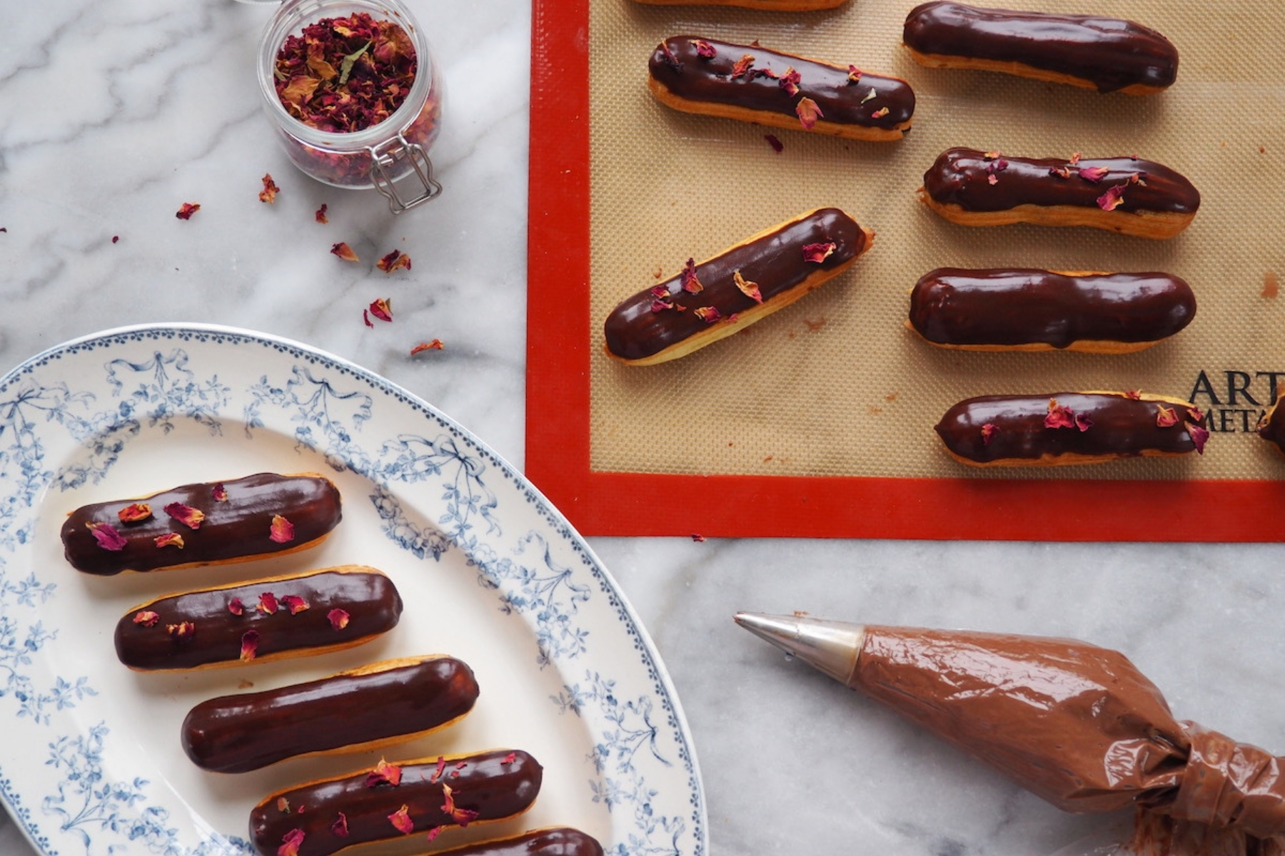 On a marble tabletop, a plate of chocolate eclair with rose petals on top.
