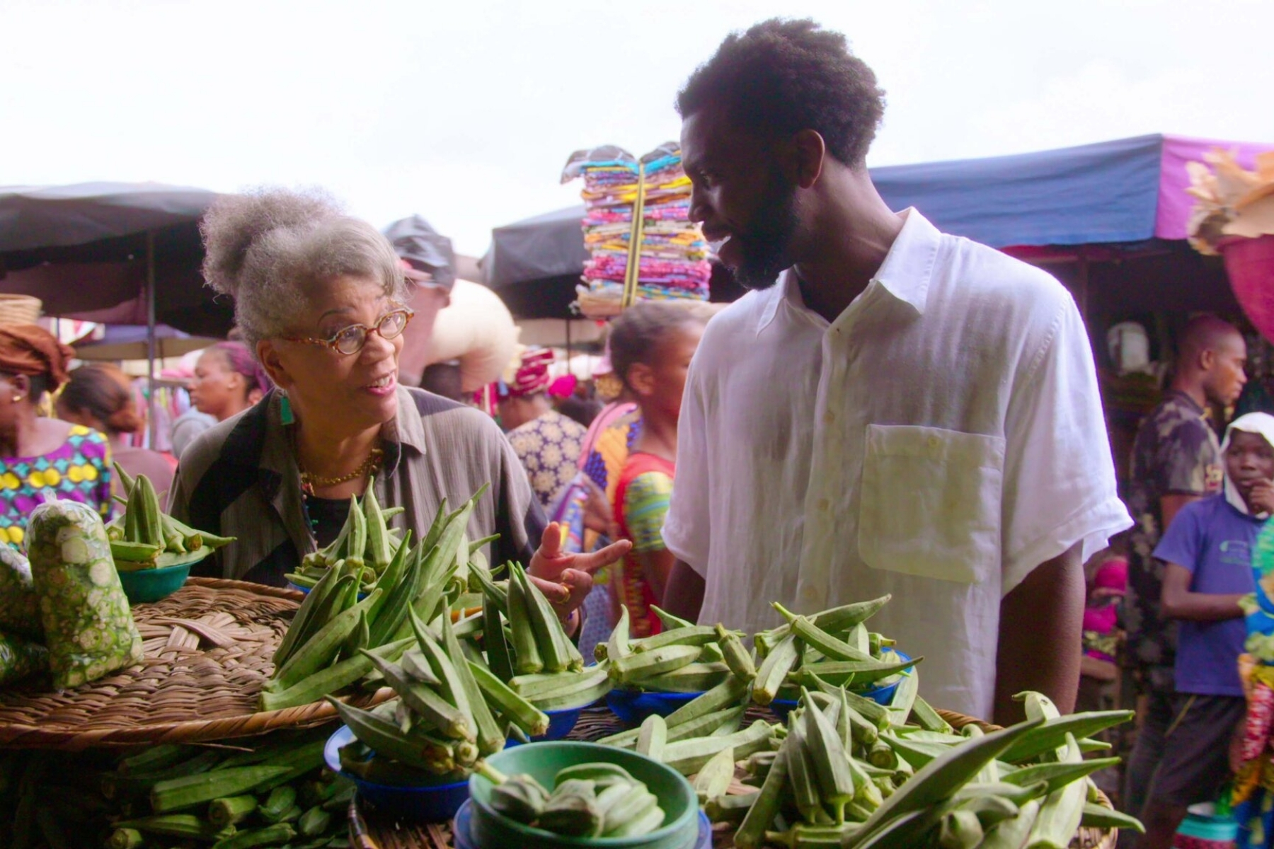 Culinary historian Jessica B. Harris and High on the Hog host Stephen Satterfield stop in front of an okra stand at the Dantokpa Market in Cotonou, Benin. The Netflix series is based on Harris’s 2011 book of the same name.