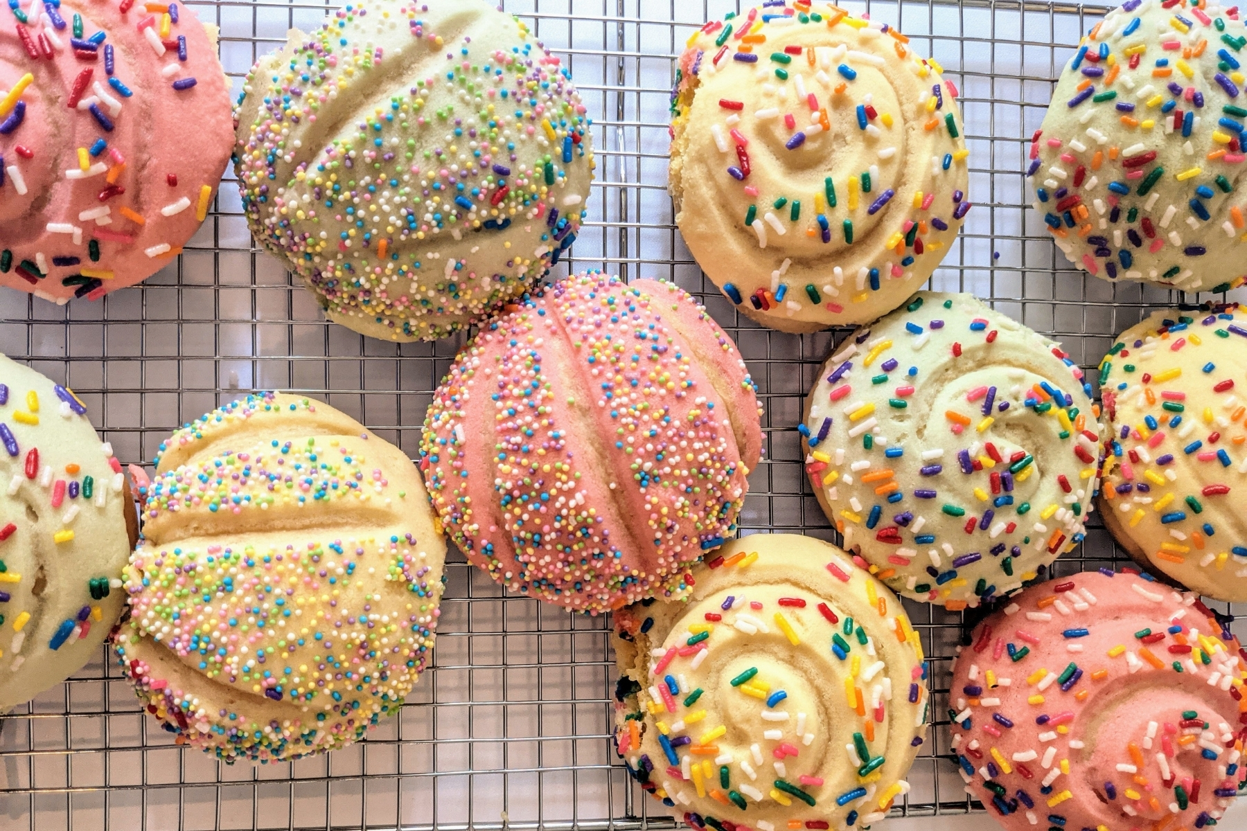 A tray of birthday cake conchas on a cooling rack.