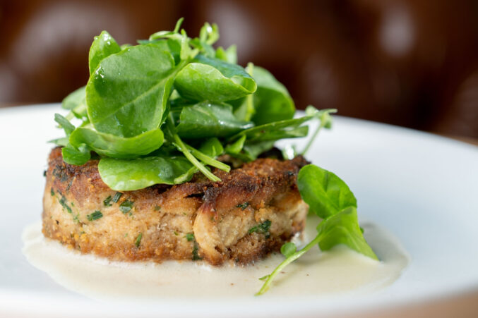 A white plate with a mushroom cake with greens on top.