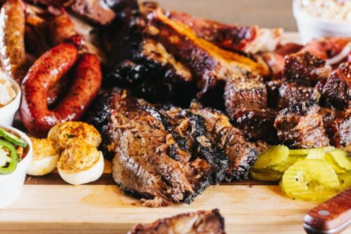 A delicious pile of Lockhart Smokehouse barbecue (brisket, links, pickles, deviled eggs) on a wood cutting board.