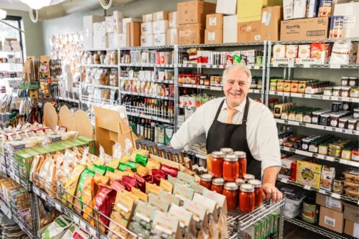 Caterer Ari Lowenstein stands in an aisle surrounded by foodstuffs.