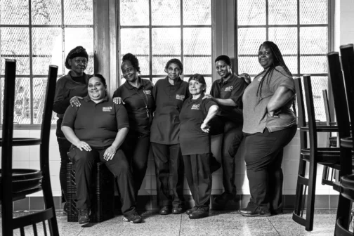 Lessie Dixon poses with her Dallas Independent School District coworkers in front of school cafeteria windows.