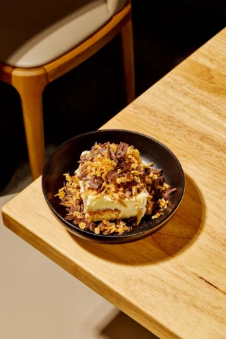 Bowl of tiramisu with crispies on table.