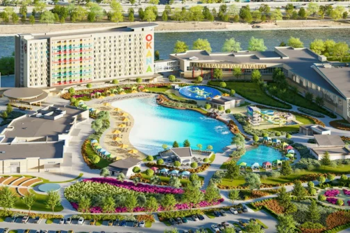 Aerial view of OKANA Resort & Indoor Waterpark in Oklahoma City, showing a large outdoor lagoon, hotel, waterslides, pools, cabanas, and recreational areas surrounded by greenery and a nearby river.